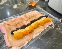 Step <p>Colocamos las pechugas abiertas y salpimentadas encima del beicon. Cojemos el turrón de jijona y lo cortamos a tiras de 1cm de ancho y por el largo de la pieza del turrón. Y la vamos a colocar encima de las pechugas en un borde . Hasta cubrir todo el ancho.</p> illustration